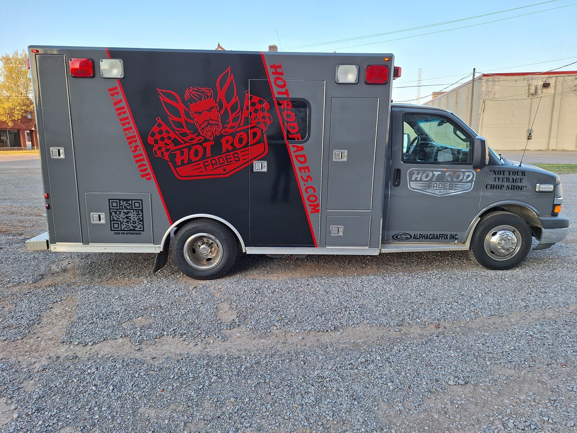 A black and red ambulance is parked in a gravel lot