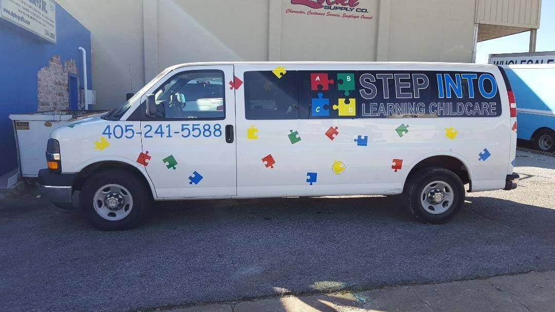 A white van with puzzle pieces painted on it is parked in front of a building.
