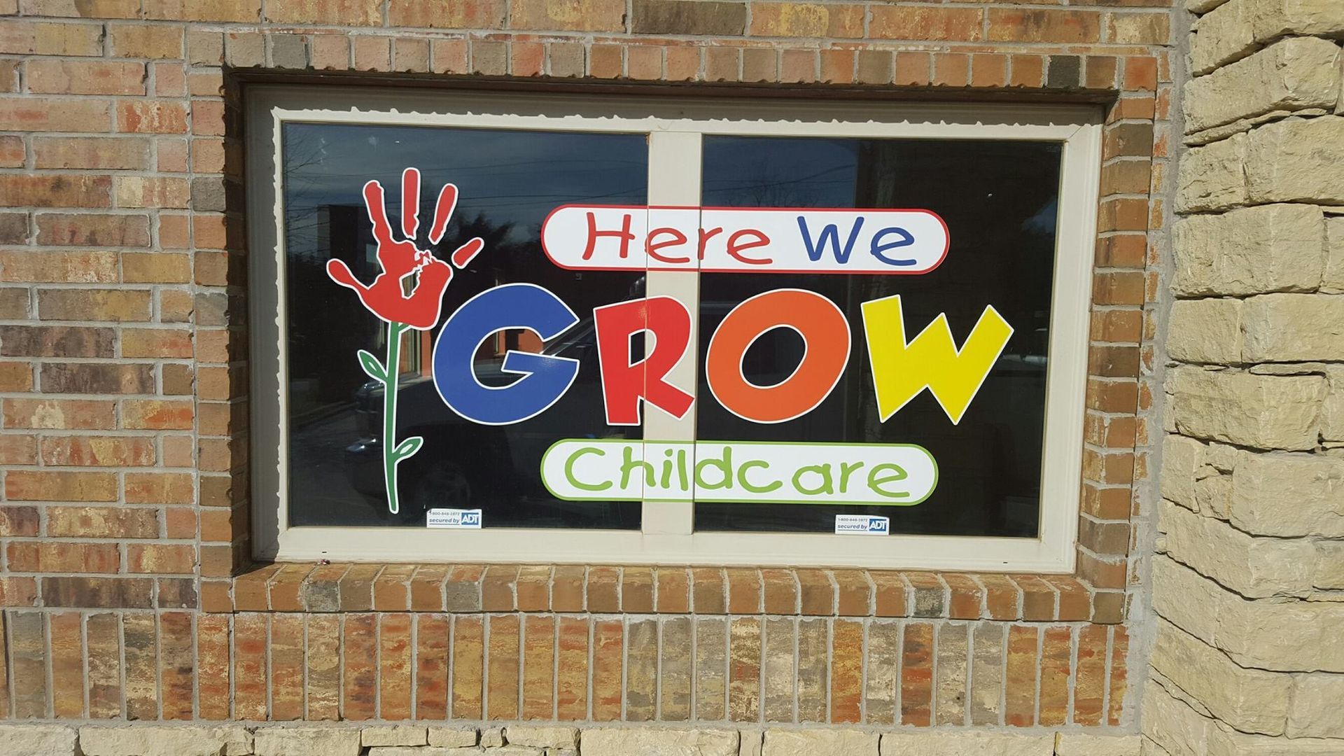 A sign on a brick wall that says here we grow childcare