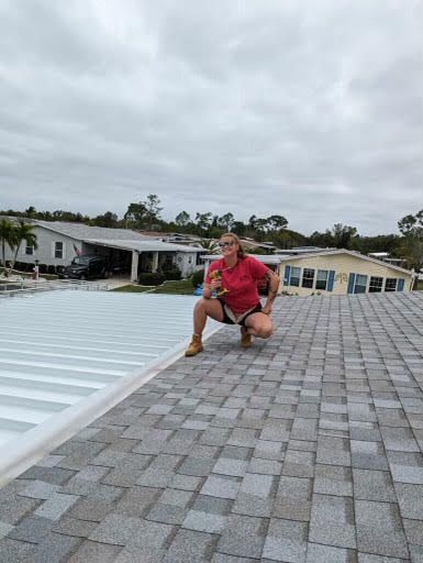 A woman is squatting on a roof with a screwdriver.