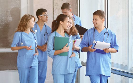 Healthcare team in blue scrubs walking together in a hospital corridor, carrying charts and smiling.