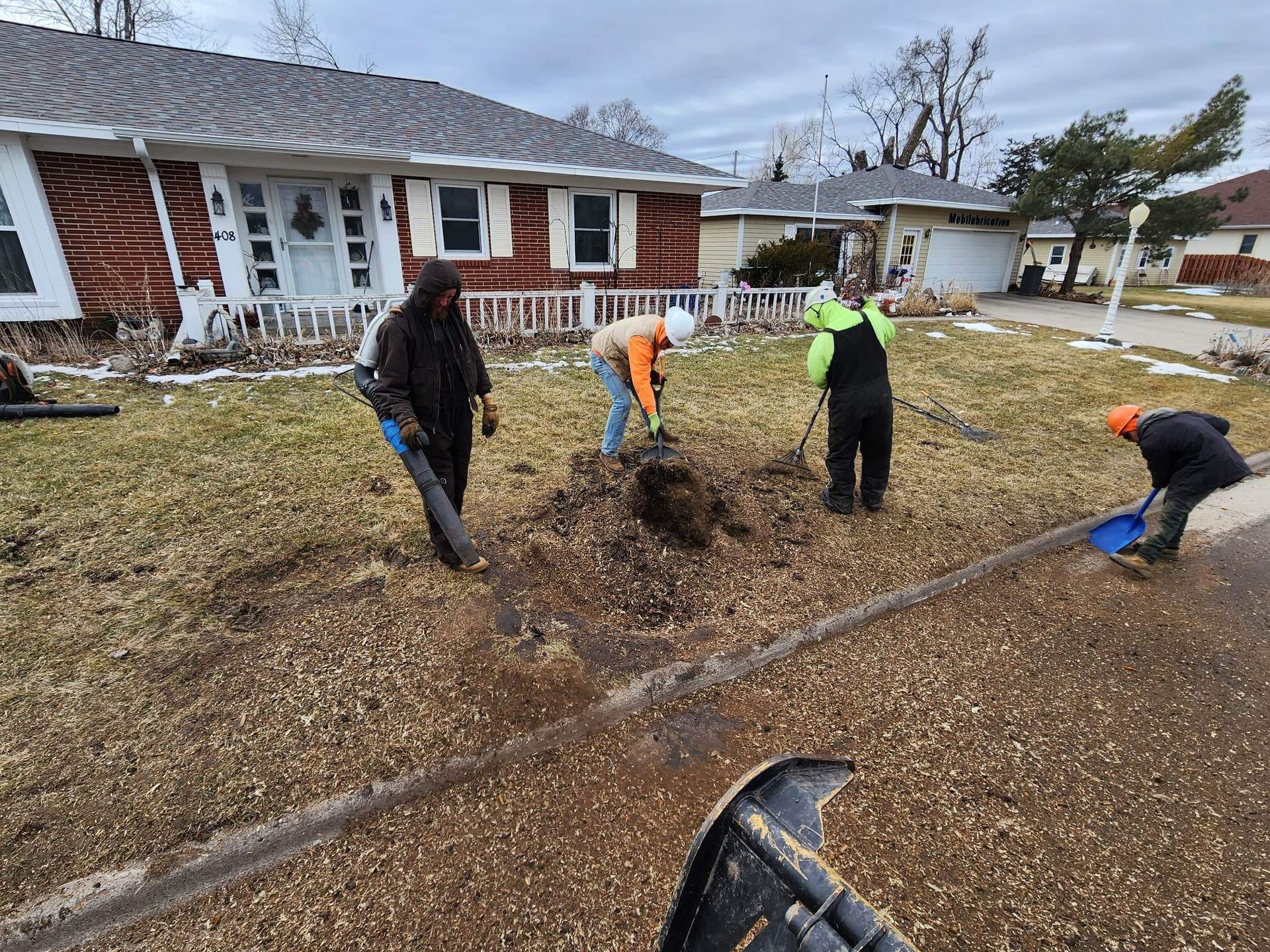 A group of people are digging in the dirt in front of a house.
