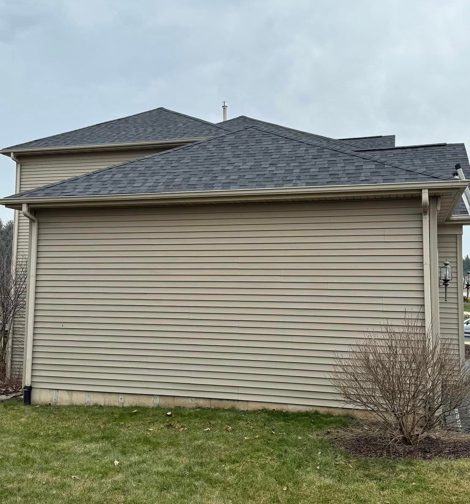 A house with a gray roof and siding is sitting on top of a lush green field