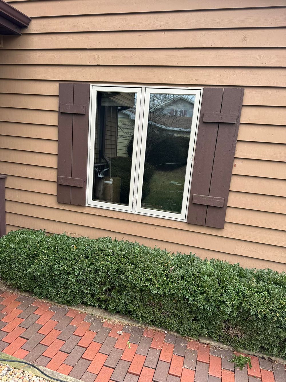 A window on the side of a house with brown shutters