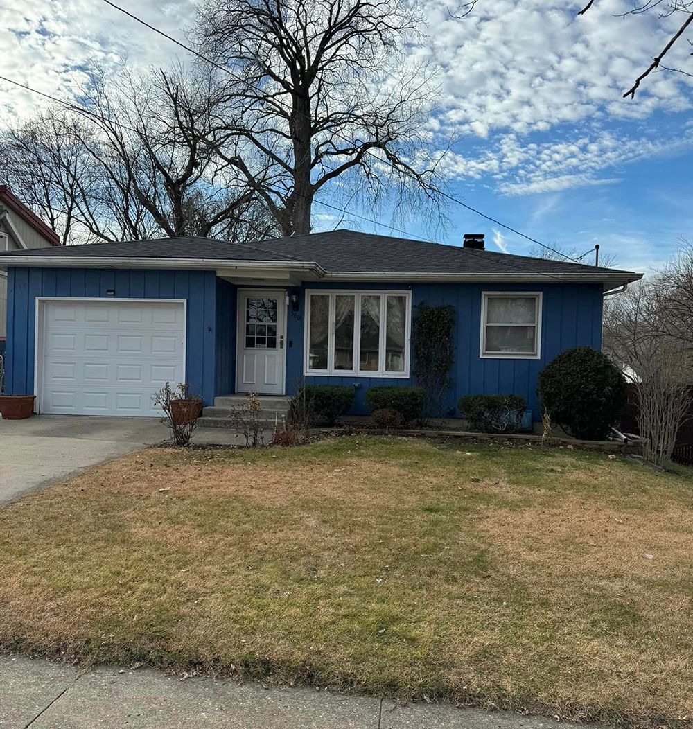 A blue house with a white garage door and a large lawn in front of it