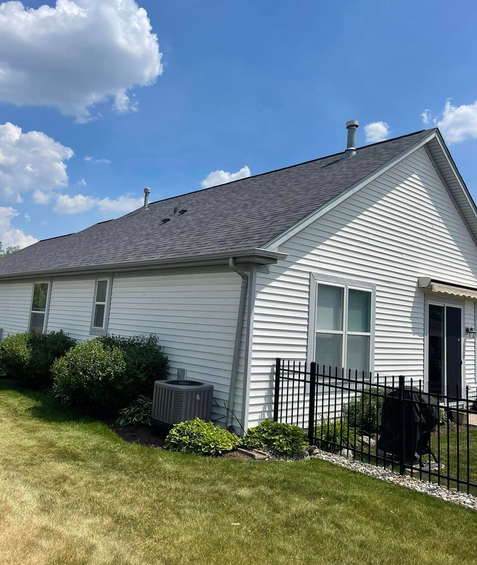 A white house with a gray roof and a fence in front of it
