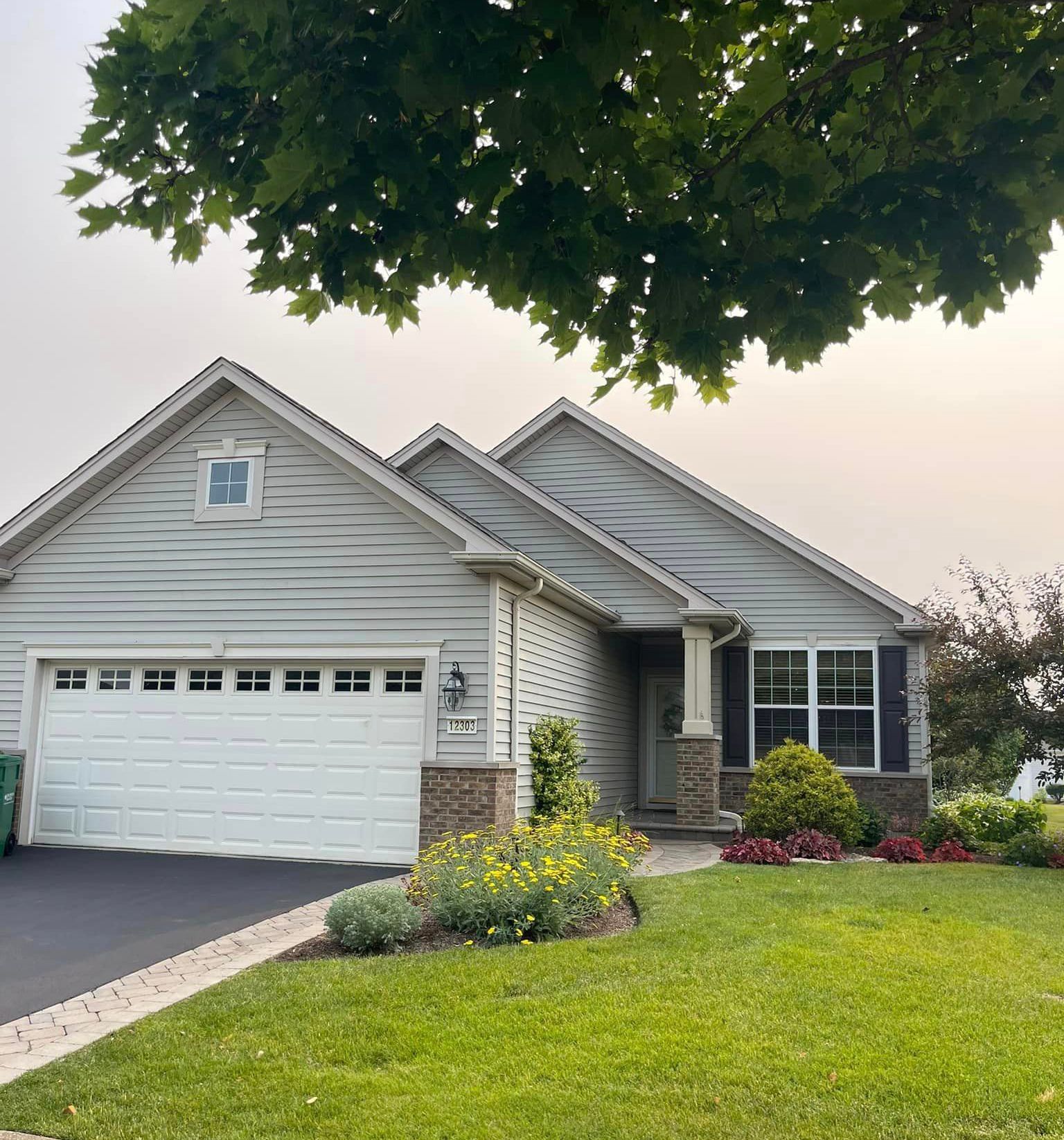 A white house with a white garage door and a tree in front of it