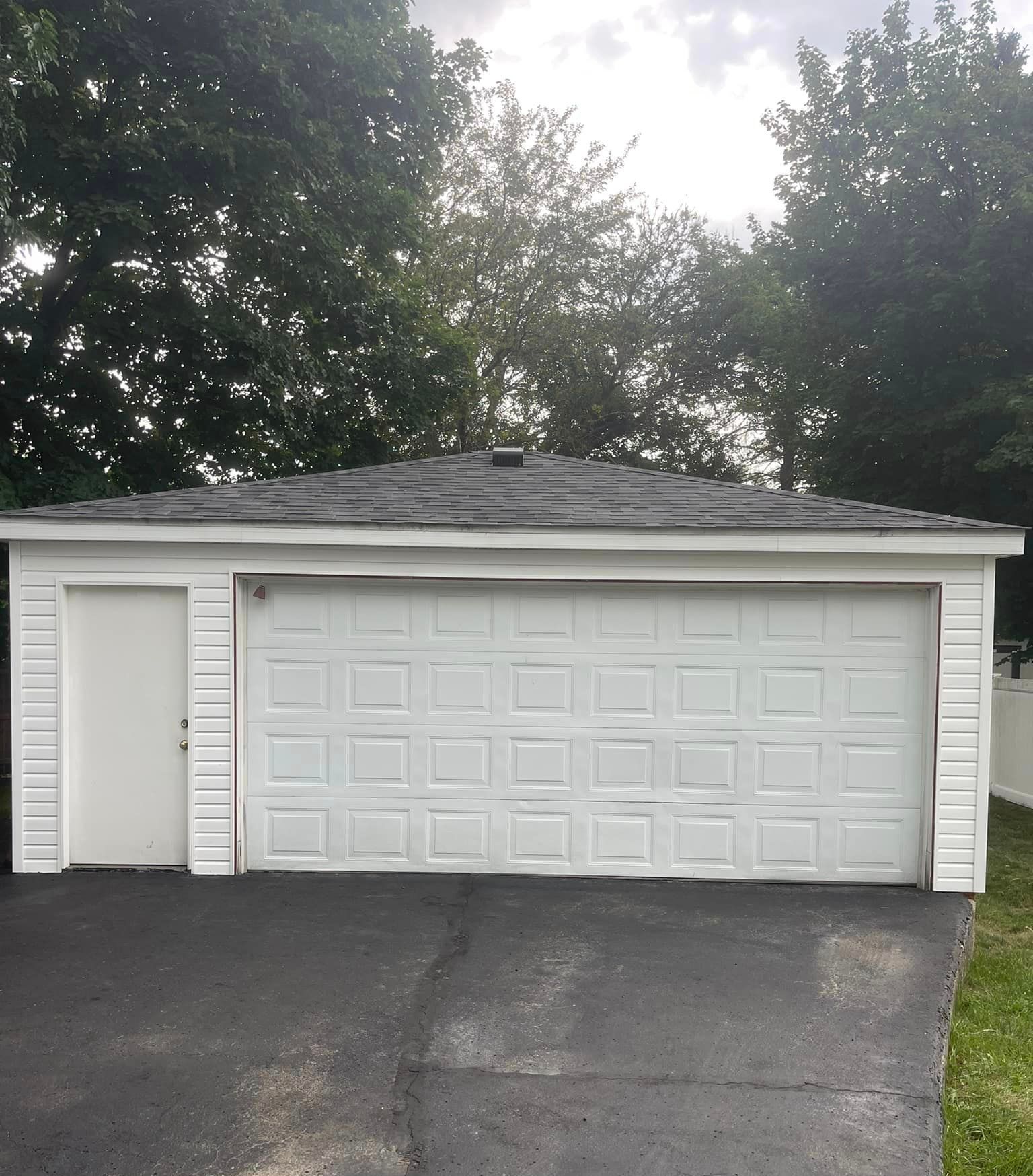 A white garage with a gray roof and trees in the background
