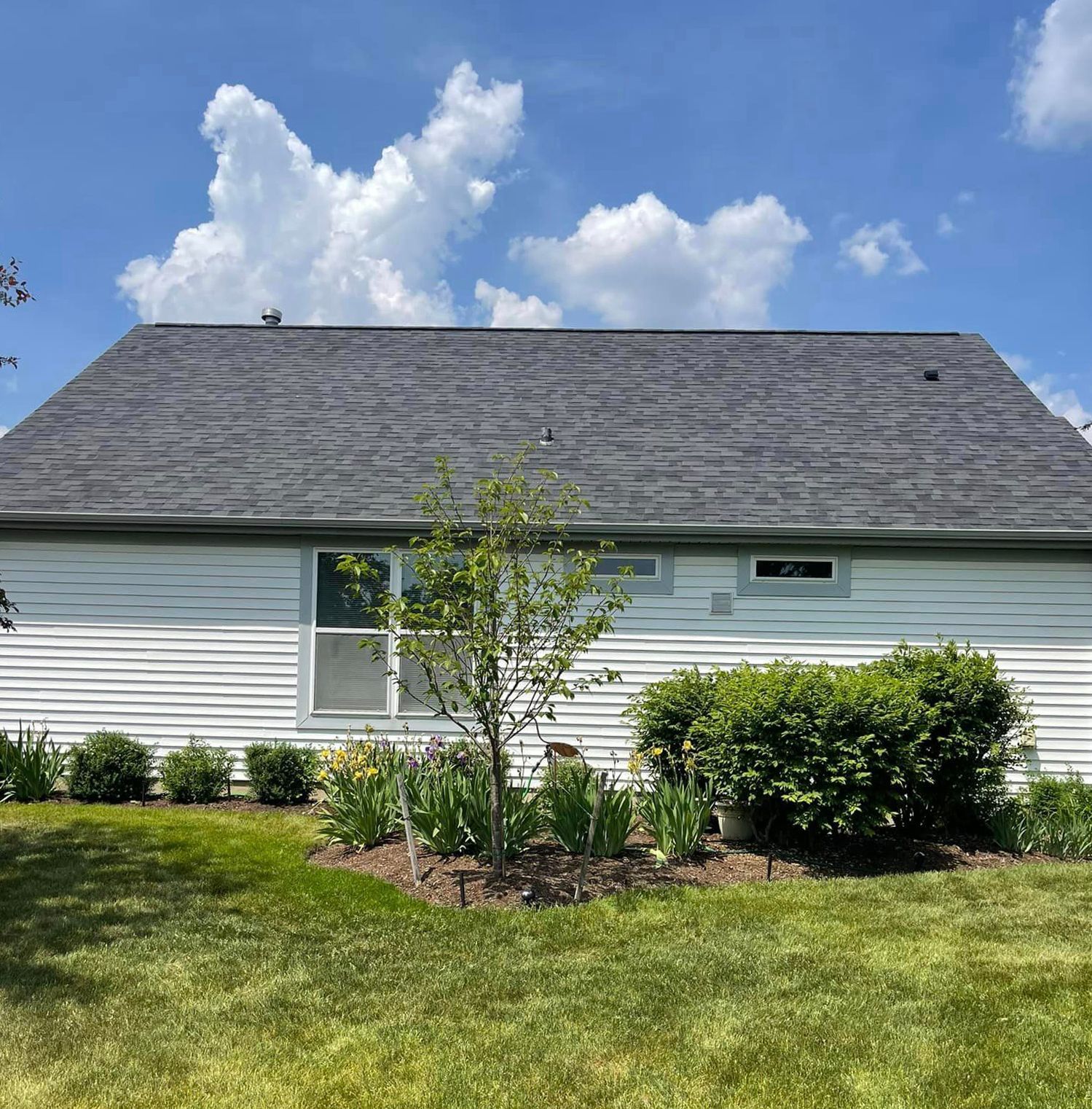 A white house with a gray roof and a lush green yard