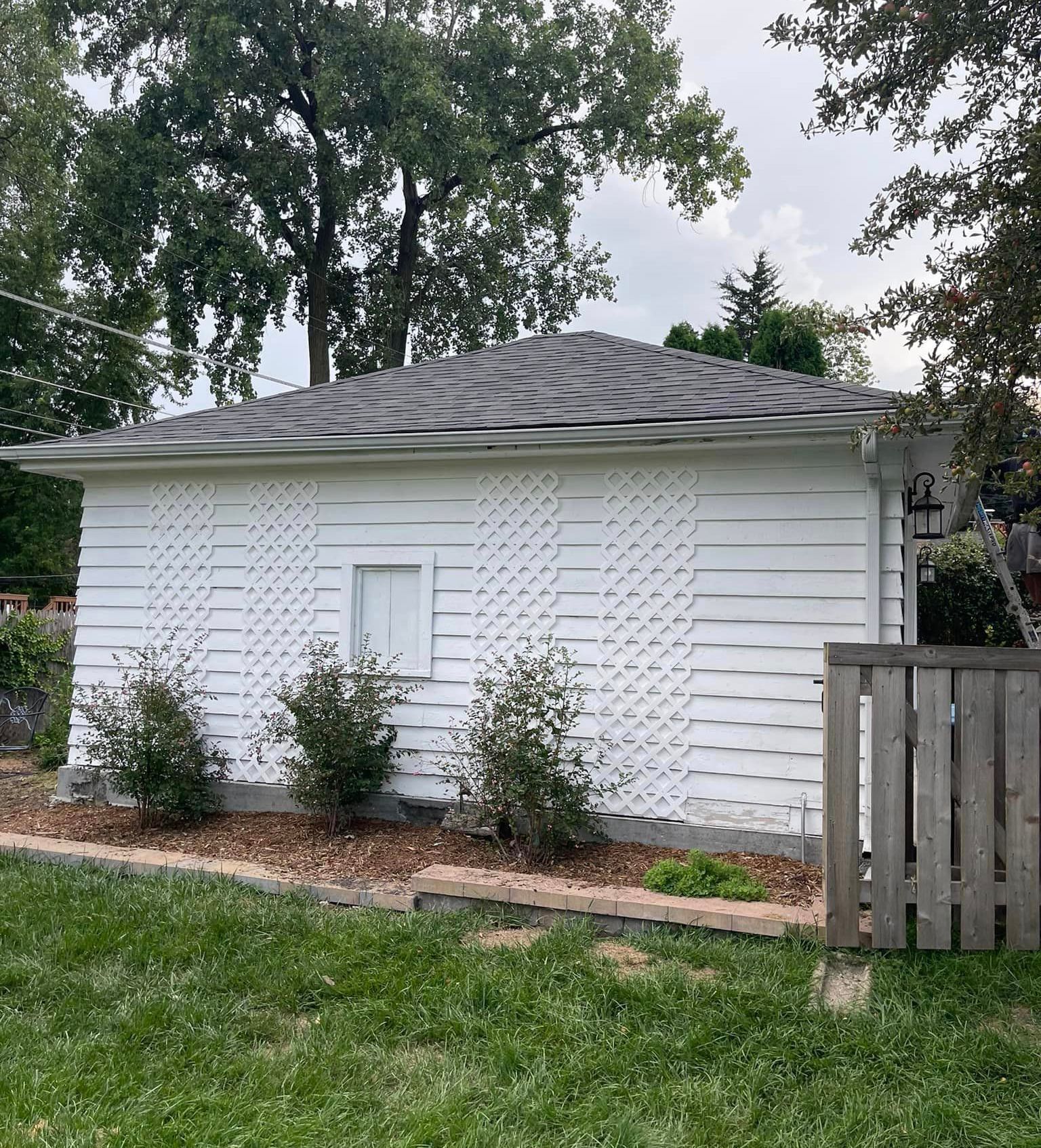 A white house with a gray roof is sitting in the middle of a lush green yard