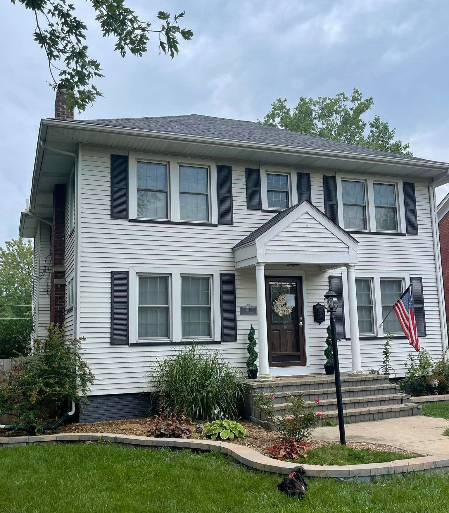 A white house with black shutters and an american flag in front of it