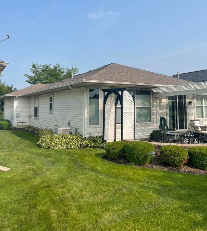 A white house with a brown roof and a large lawn in front of it