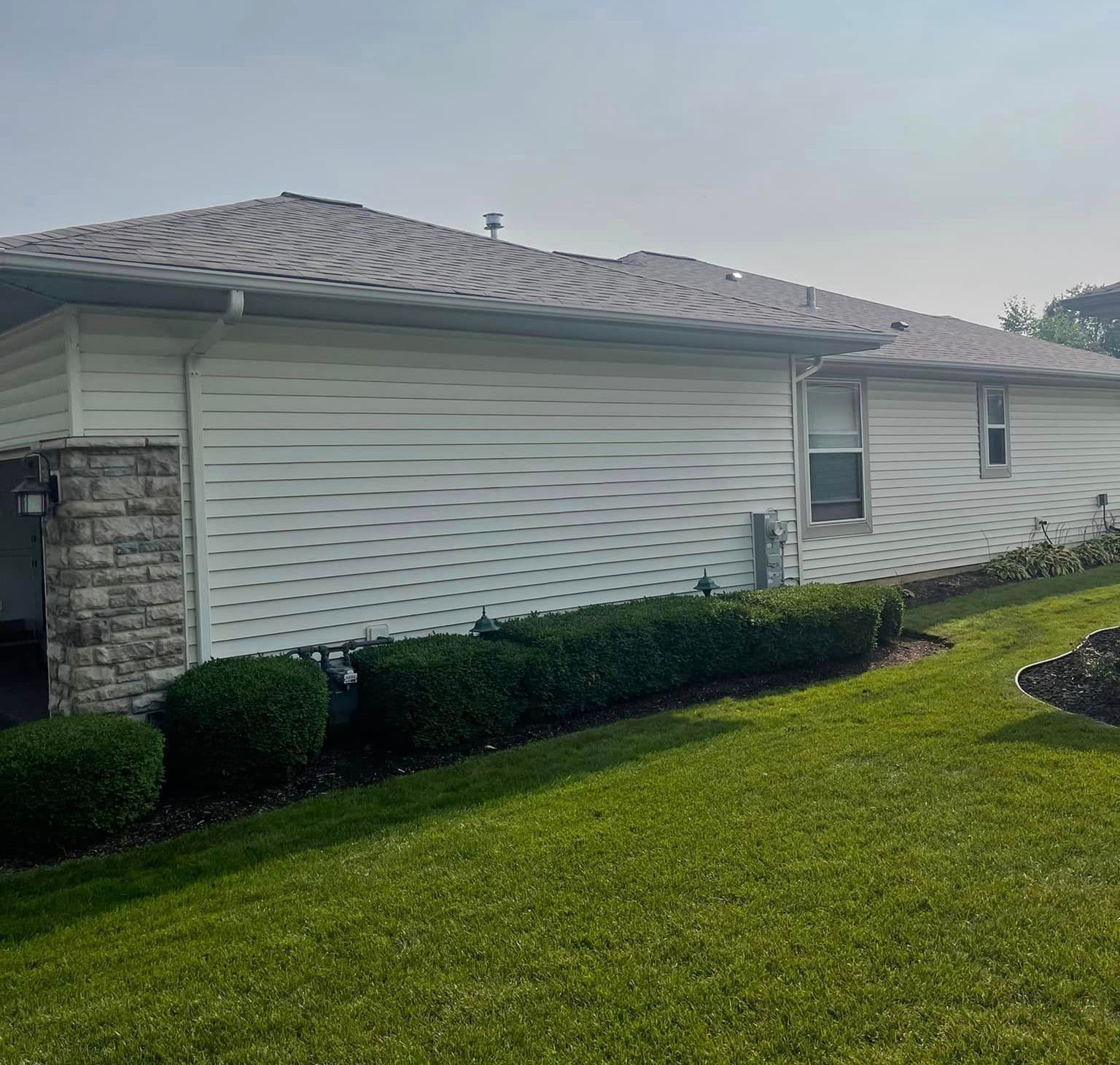 A white house with a gray roof and a lush green lawn in front of it