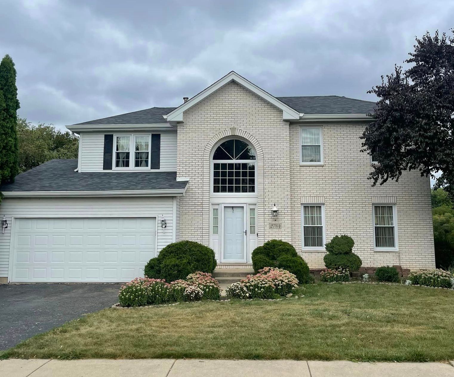 A large brick house with a white garage door and a tree in front of it