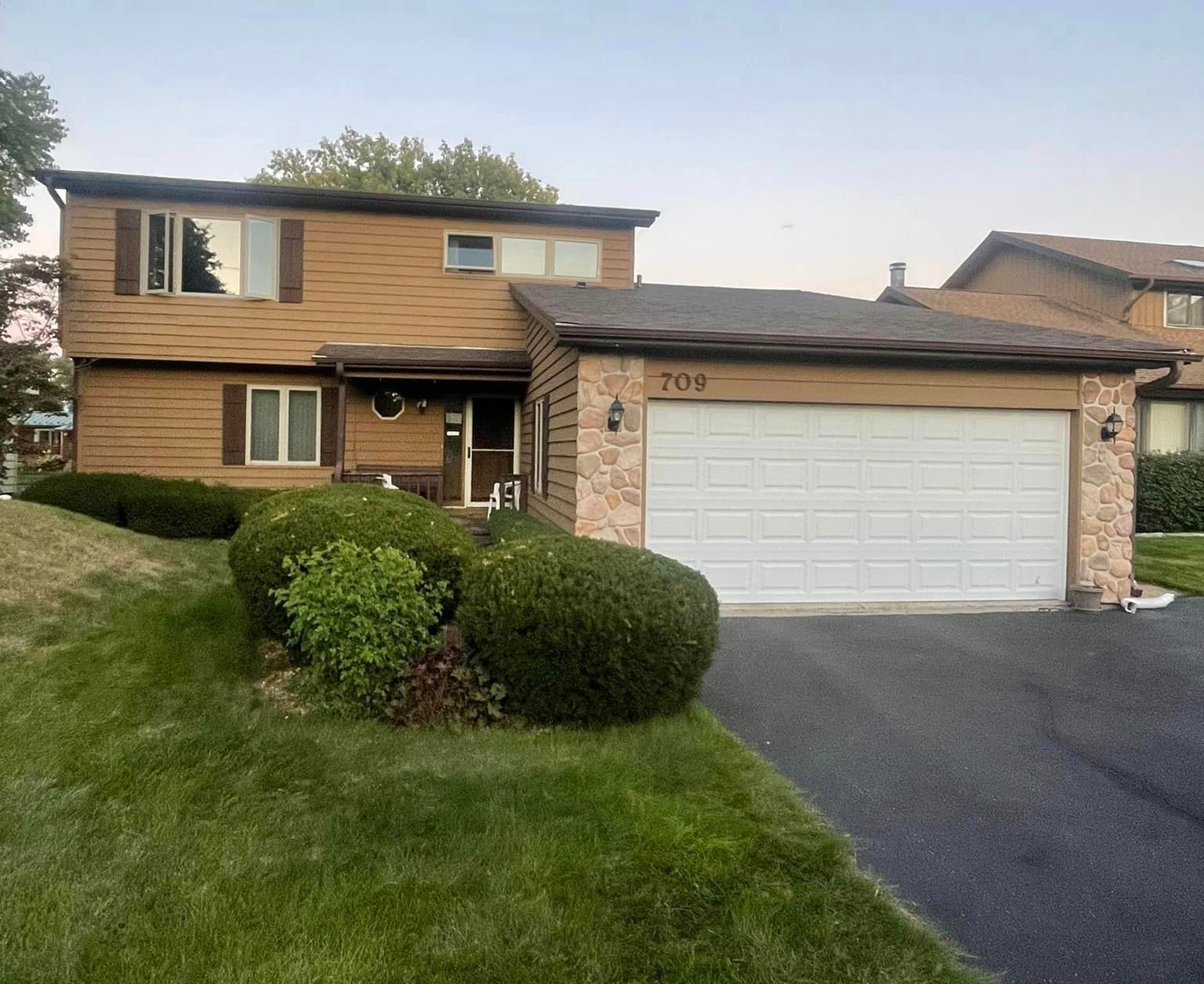 A brown house with a white garage door and a driveway