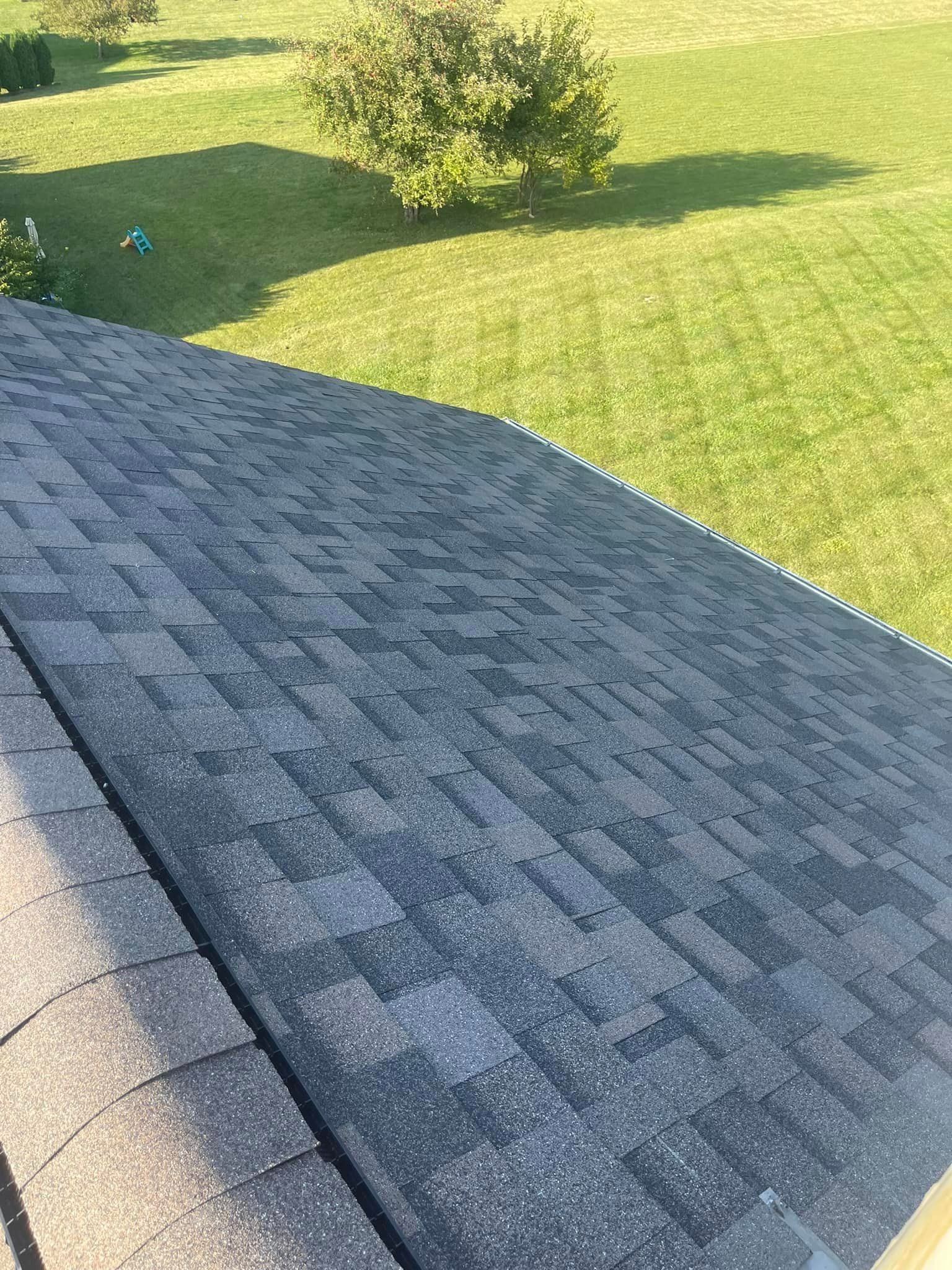 A roof with a lot of shingles on it is sitting on top of a lush green field