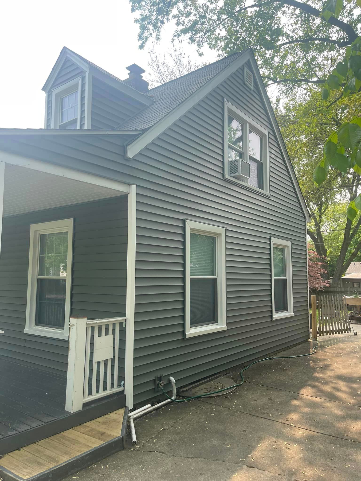 A house with a gray siding and white trim is sitting on top of a dirt field