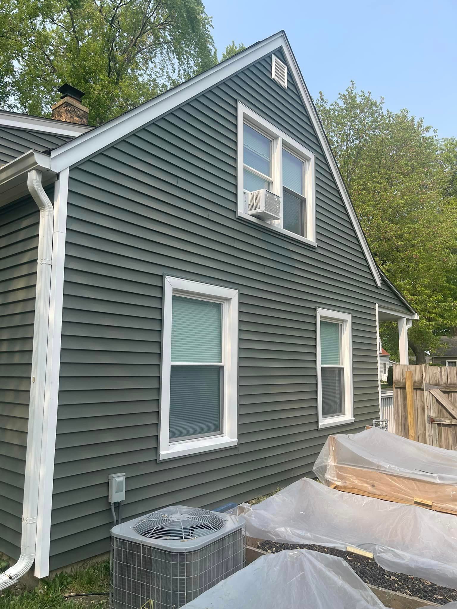 A house with a green siding and white trim is sitting next to a greenhouse