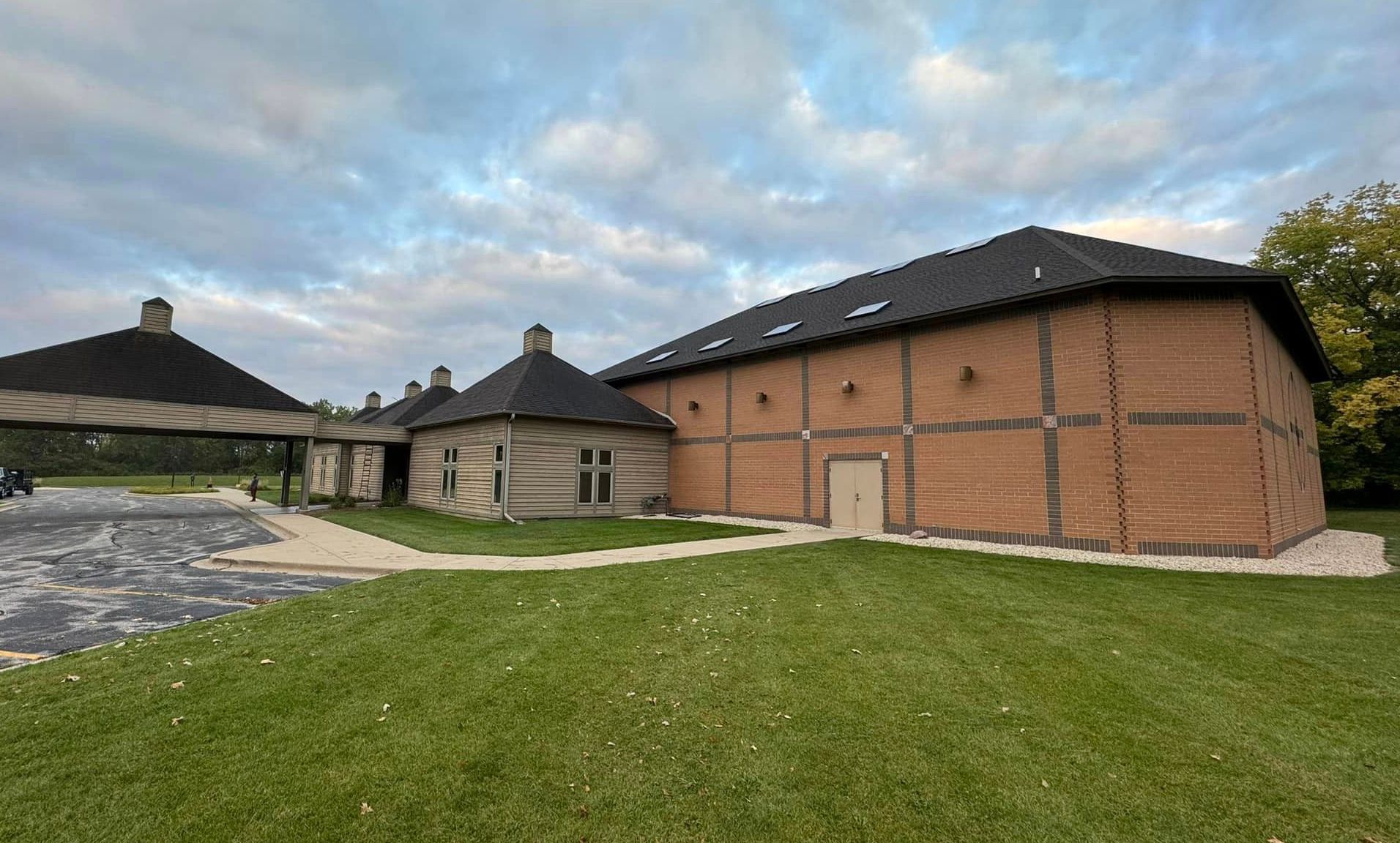 A large brick building with a black roof is sitting on top of a lush green field