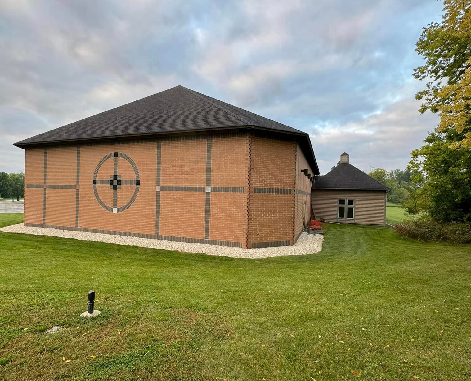 A large brick building with a black roof is sitting in the middle of a lush green field
