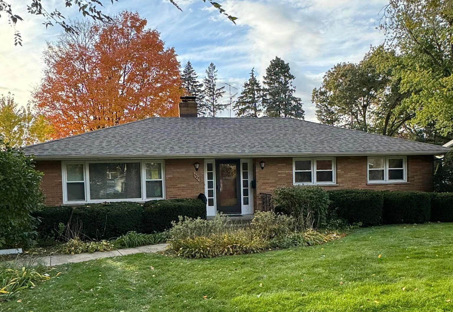 A brick house with a gray roof and a large lawn in front of it