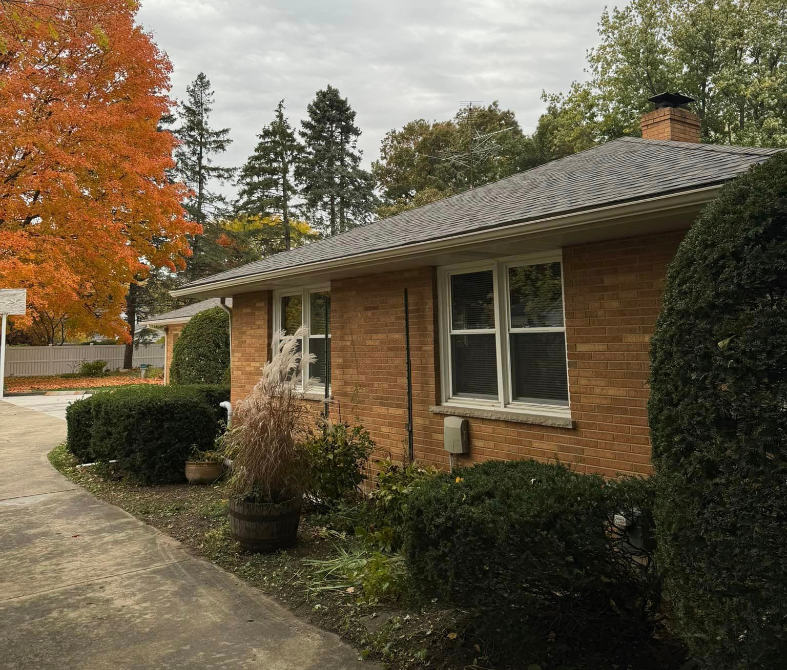 A brick house with a gray roof is surrounded by bushes and trees