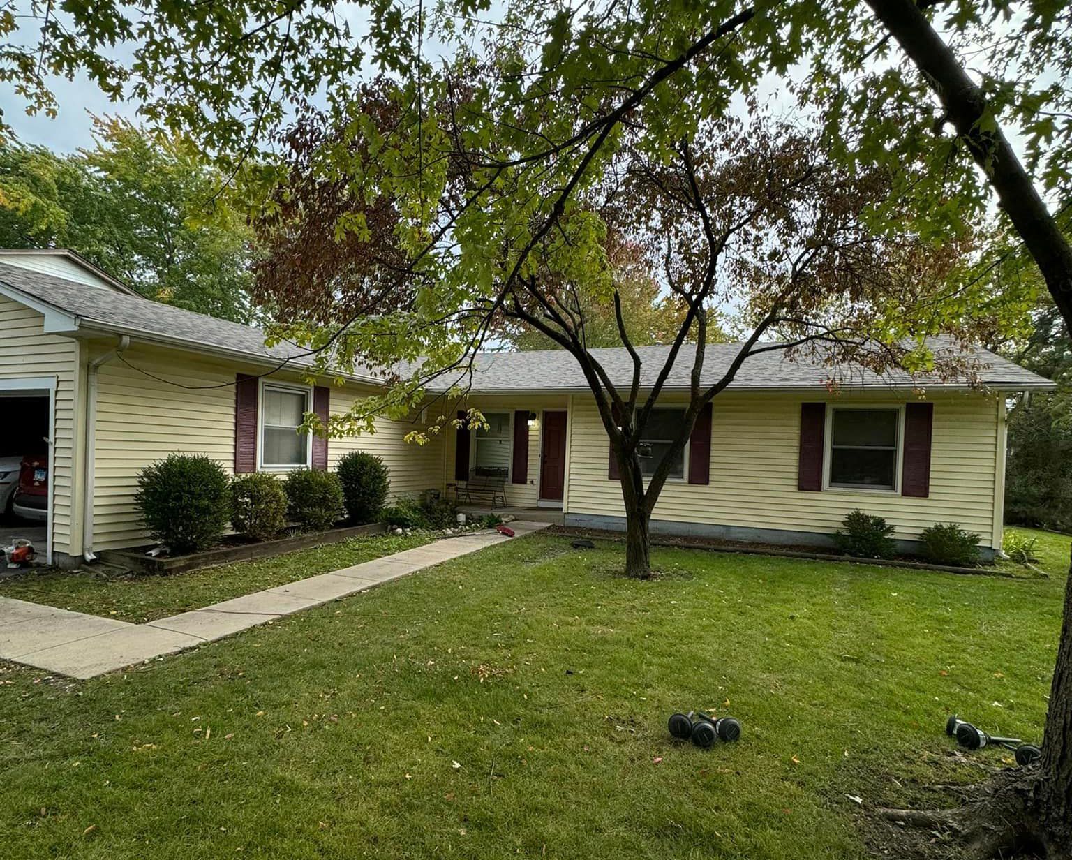 A yellow house with red shutters and a tree in front of it