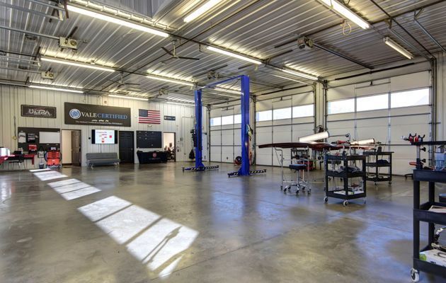 Brightly lit auto repair shop with lift, equipment, and open bay doors.