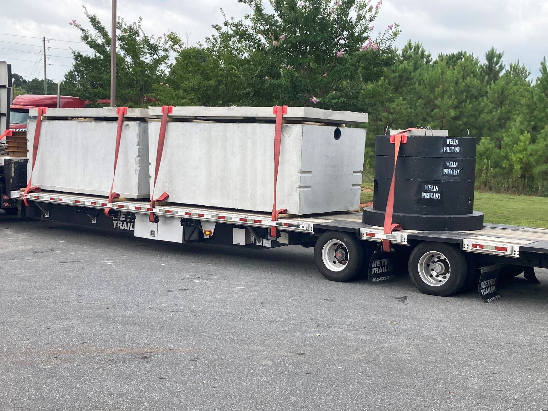 Flatbed trailer hauling white wrapped cargo and a black container on a truck lot