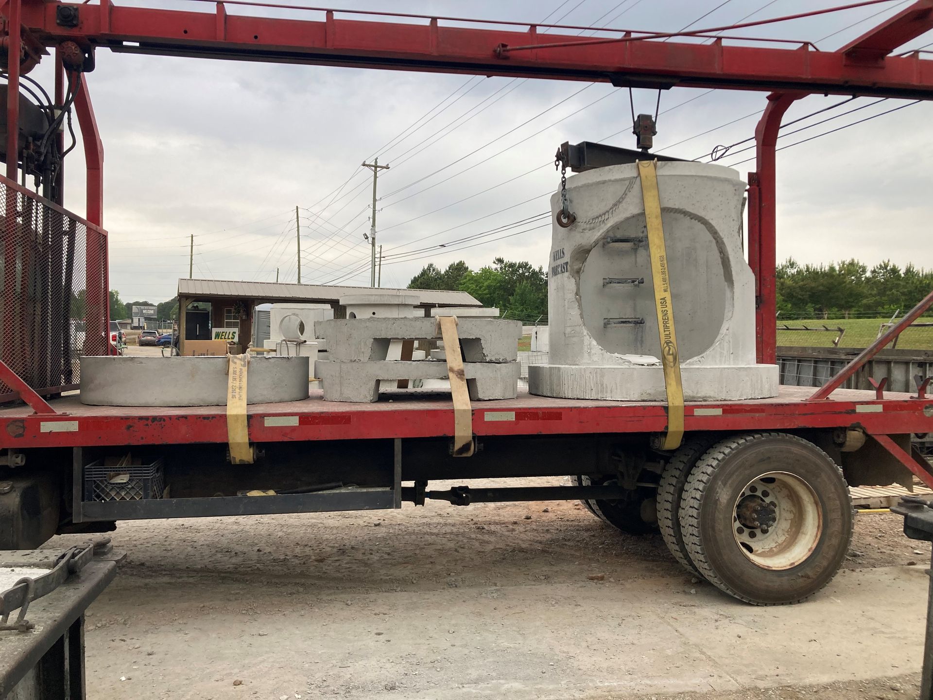 Red flatbed trailer carrying large gray industrial equipment strapped down with yellow tie-downs outdoors