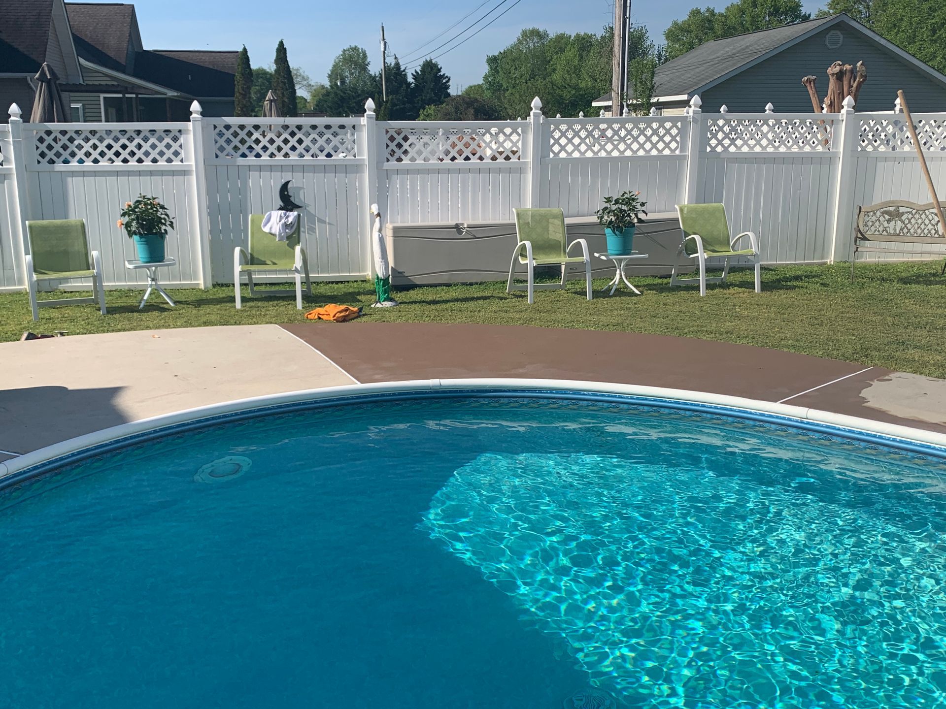 Above-ground pool in backyard, green chairs by a white fence. Sunny day.