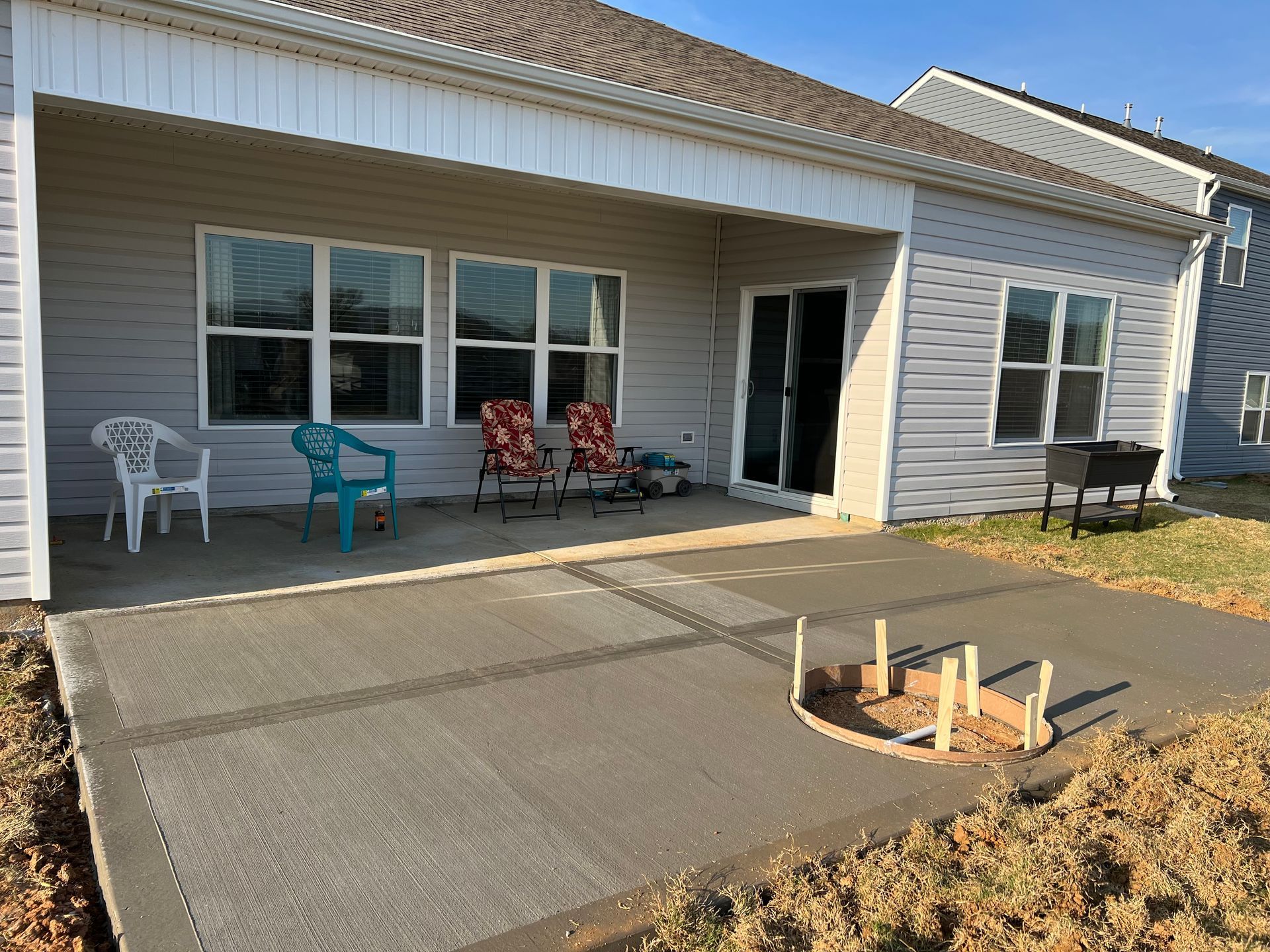 Back patio with fresh concrete, outdoor seating, and a grill. House in the background.