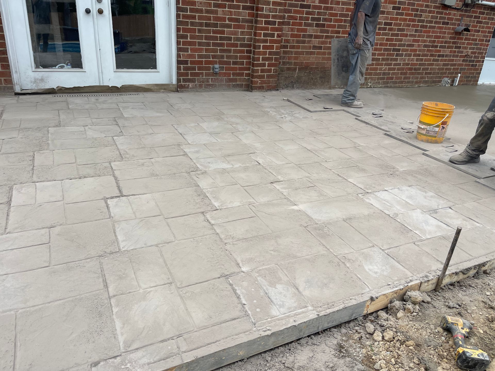 Workers laying paving stones on a patio next to a brick building.