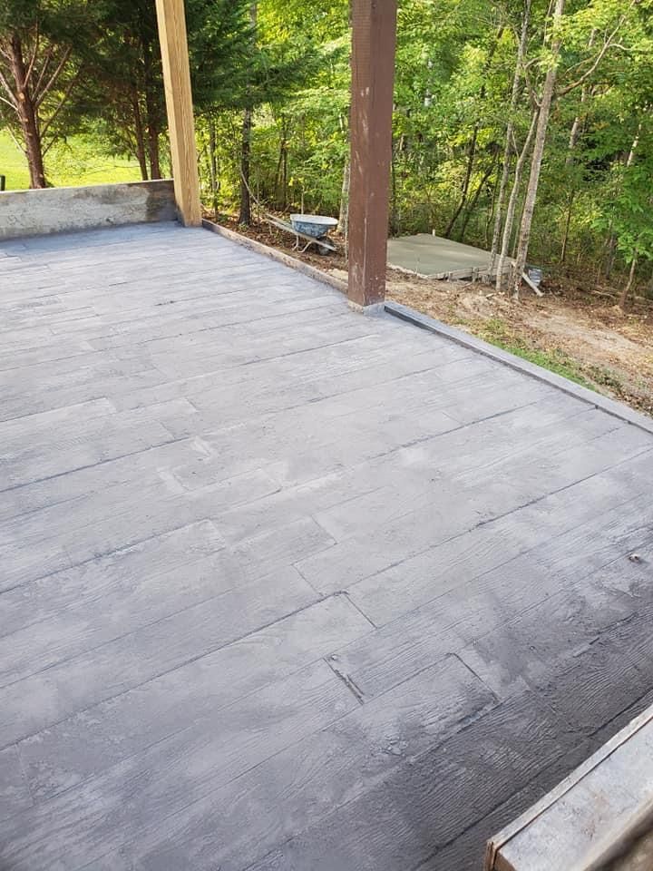 Gray concrete patio with wood-like texture and brown support beams in a wooded outdoor setting.