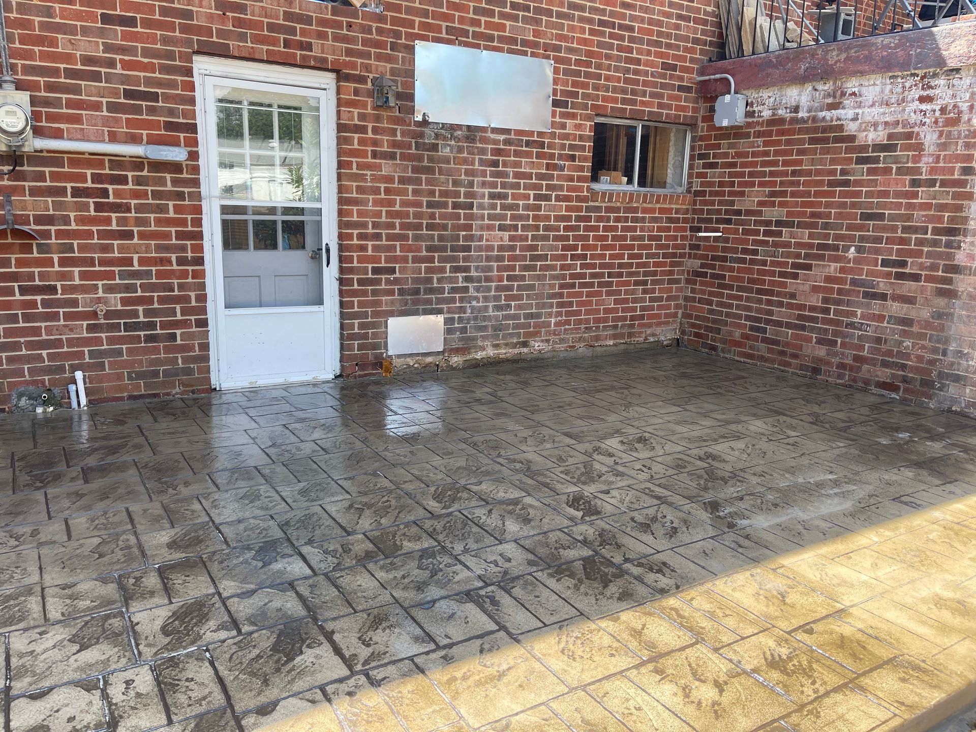 Brick-walled outdoor patio with wet, stamped concrete flooring; a white door and small window are visible.