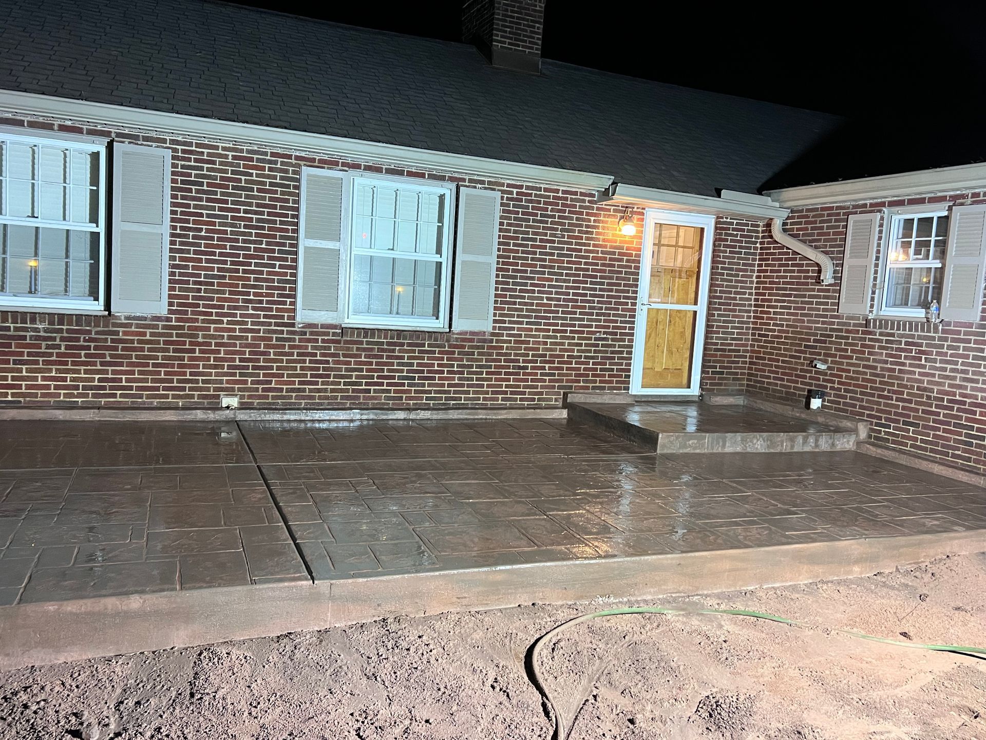 Brick house exterior with a paved patio and steps leading to the front door; night.