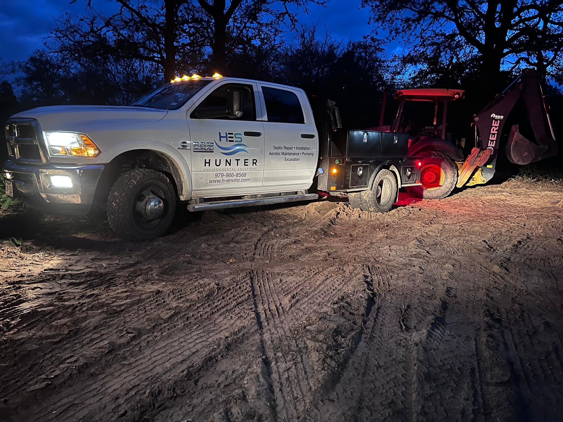 A white truck is parked in the dirt next to a red tractor.