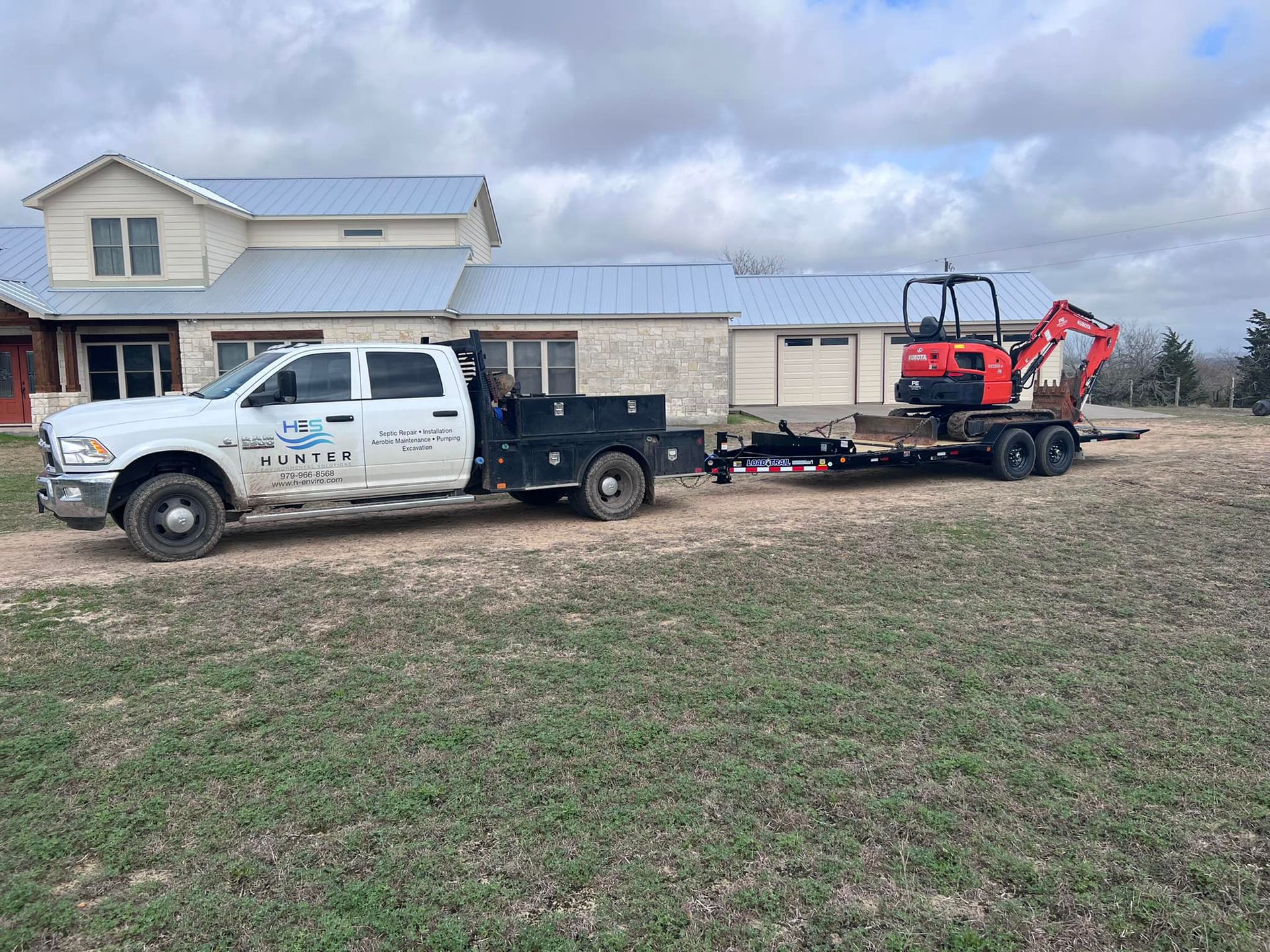 A white truck is towing a small excavator on a trailer.