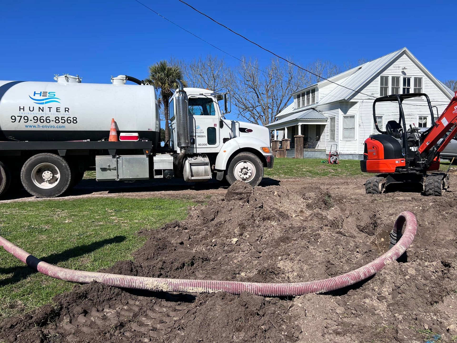 A white truck with a hose attached to it is parked in front of a house.