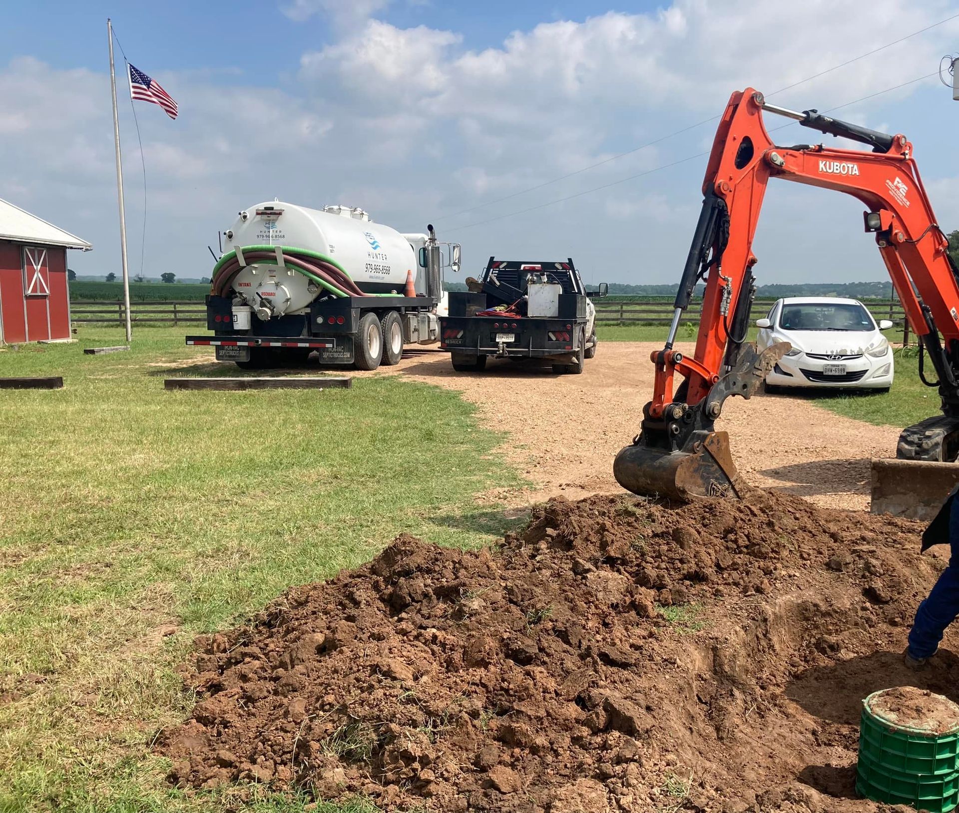 An excavator is digging a hole in the dirt next to a tanker truck.