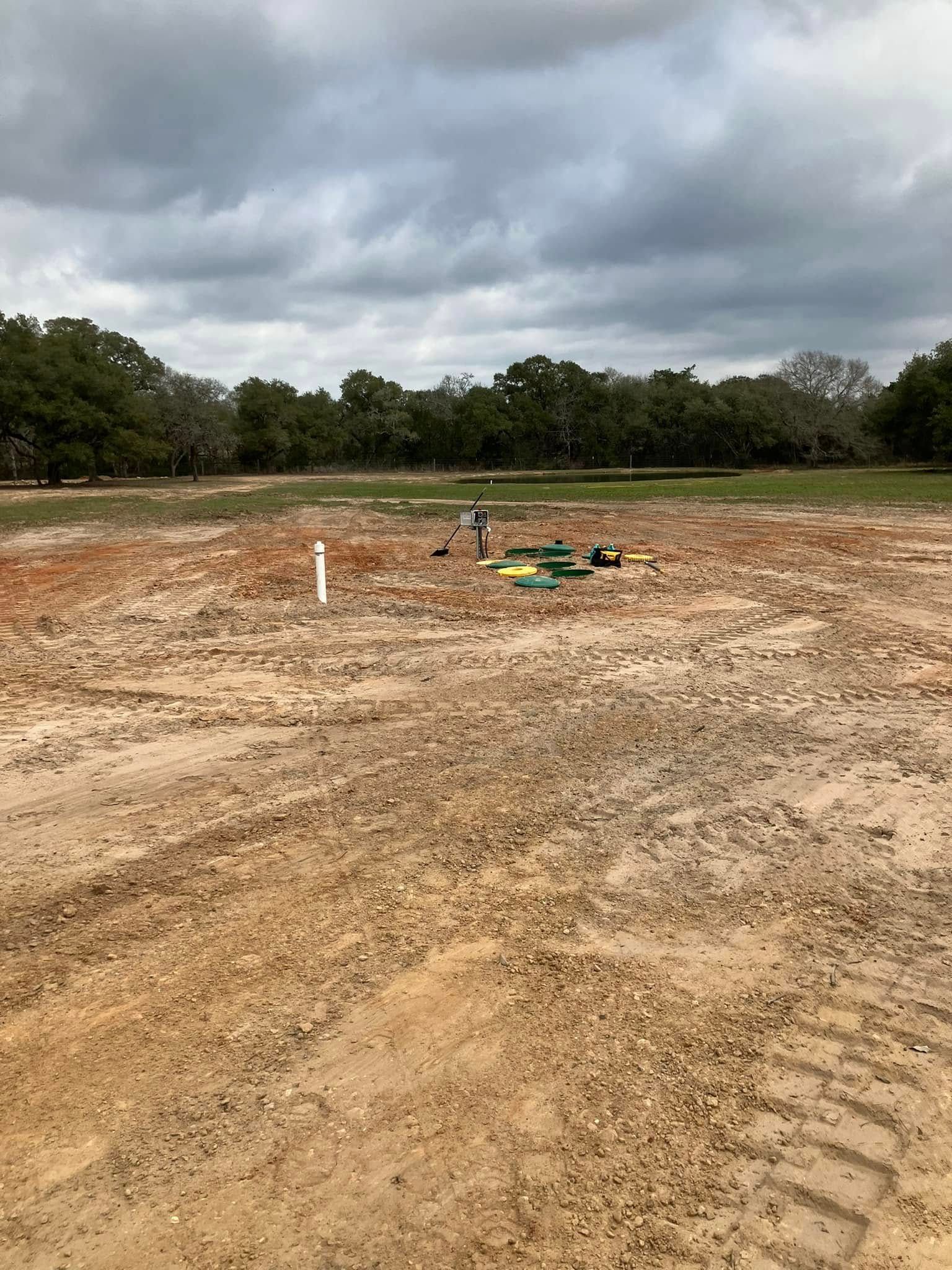 A dirt field with trees in the background and a cloudy sky.