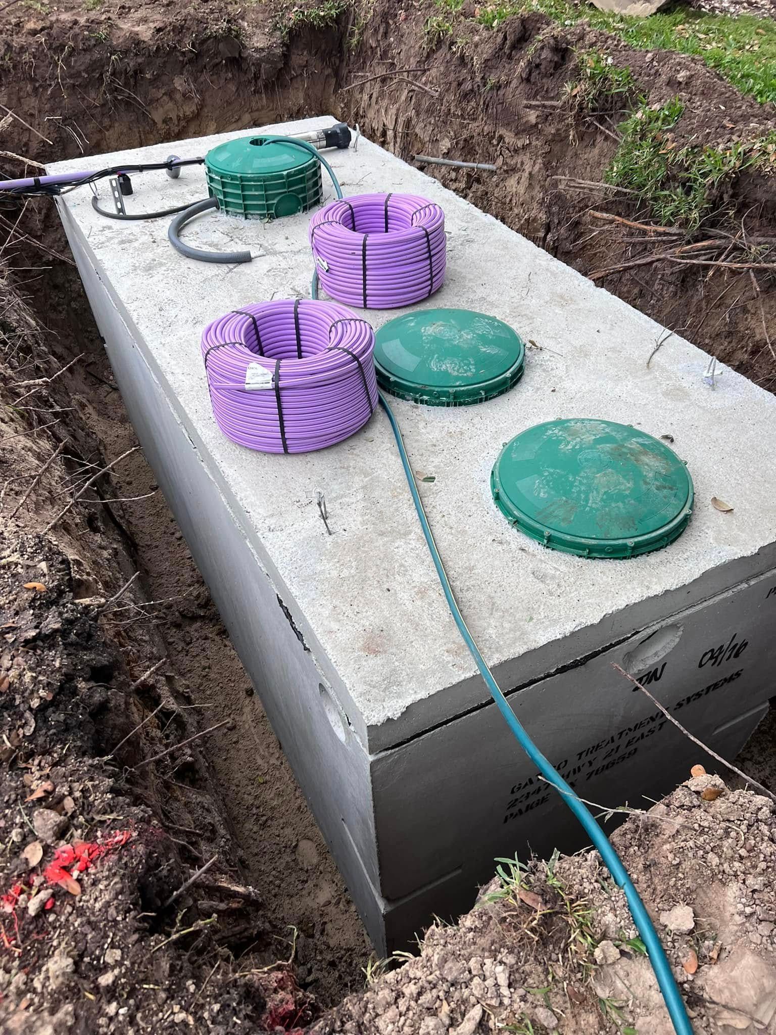A large concrete septic tank is sitting in the dirt next to a hose.