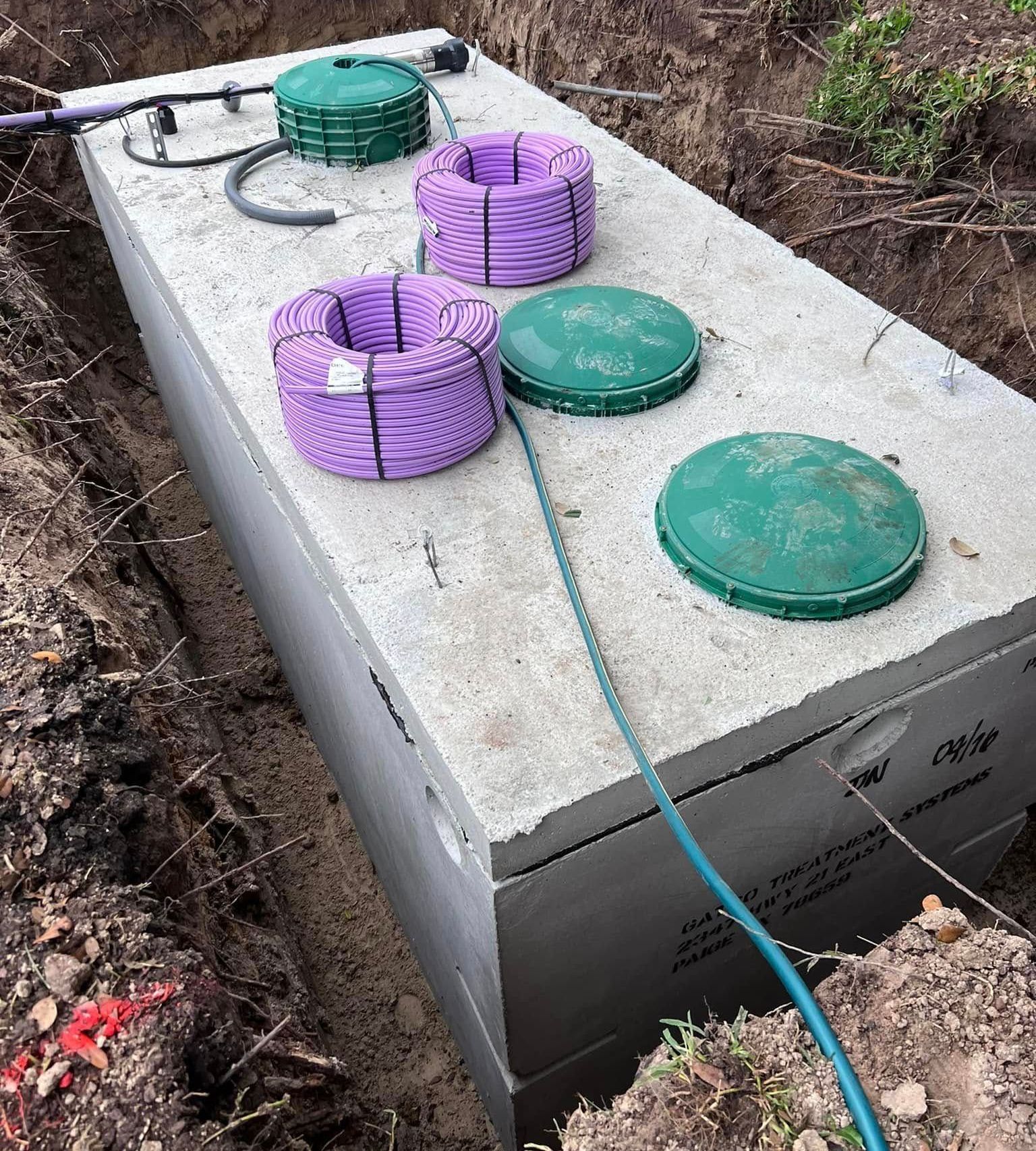 A large concrete tank with purple ropes and green lids is sitting in the dirt.