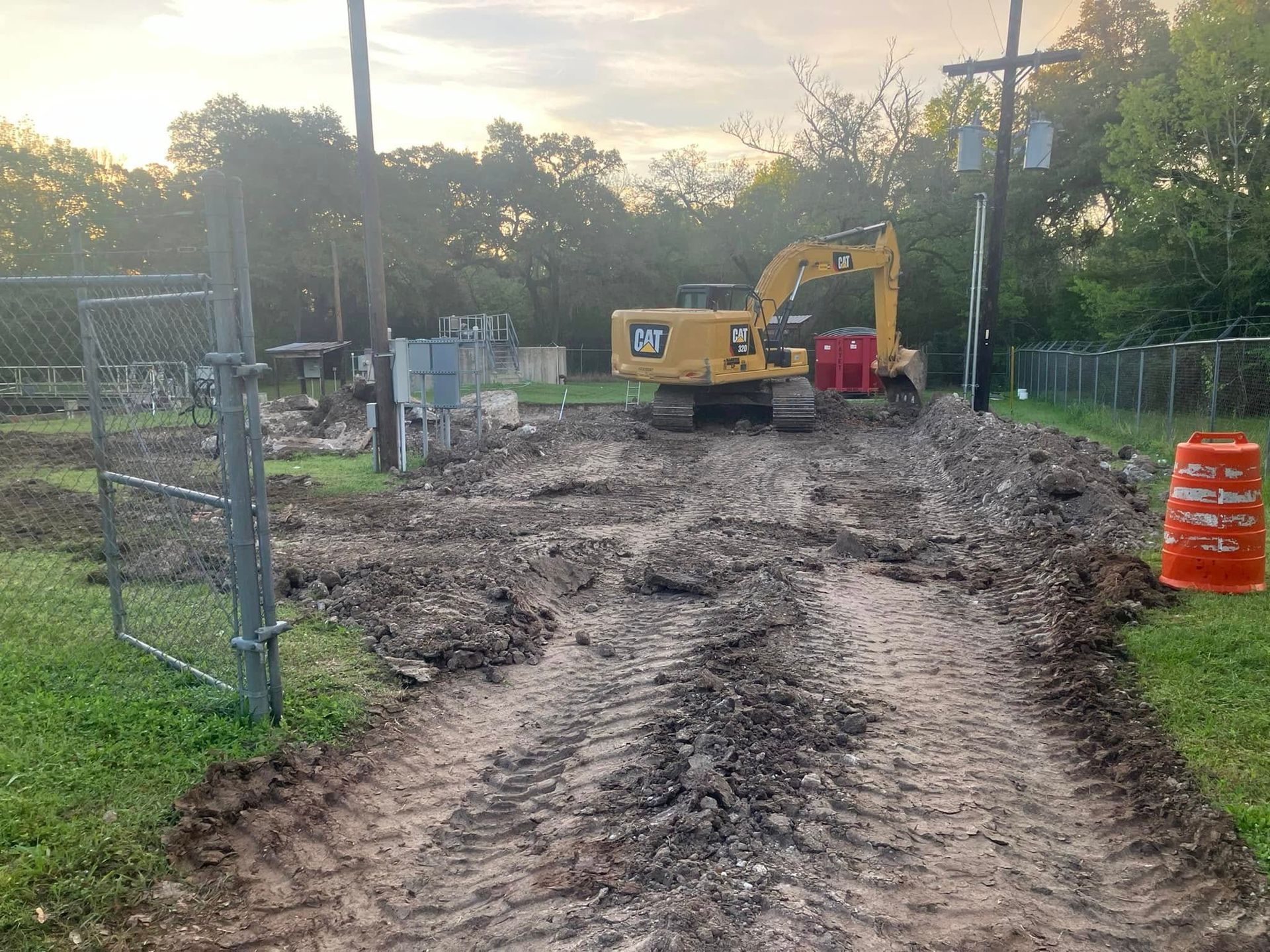 A bulldozer is driving down a dirt road next to a fence.