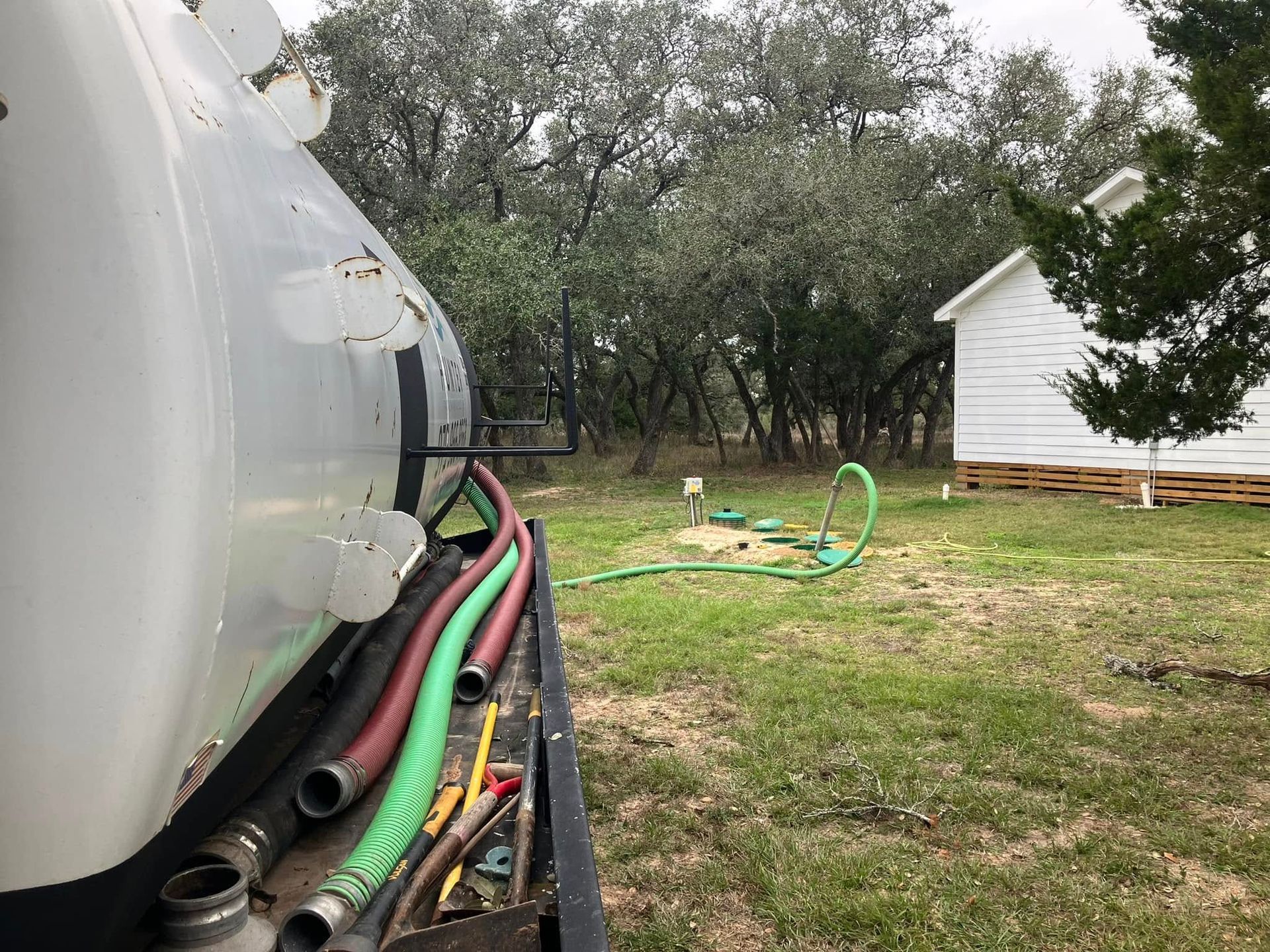 A vacuum truck is parked in a grassy field next to a house.
