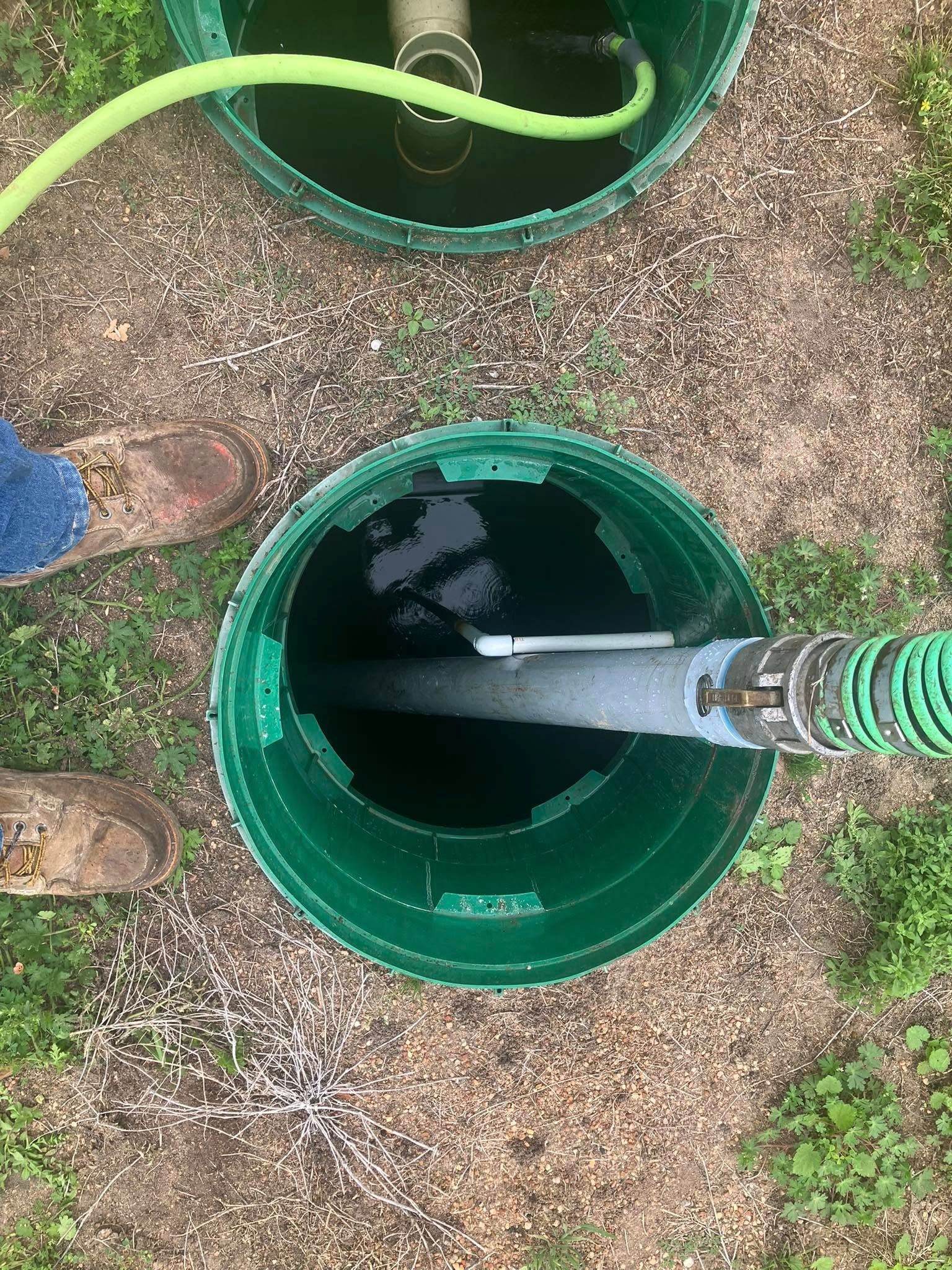 A person is pumping water into a septic tank with a green hose.