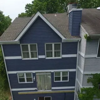 A blue-sided three-story house with white trim and a gabled roof, viewed from an elevated angle.