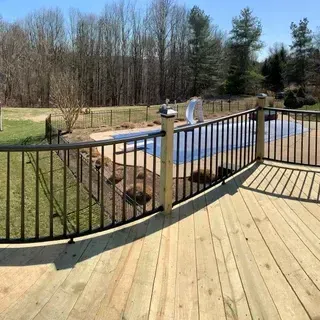A wooden deck with a curved black metal railing overlooking a backyard pool covered with a blue tarp.