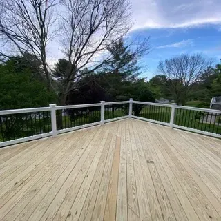 A newly built wooden deck with white railings and black balusters overlooking a leafy backyard under a partly cloudy sky.