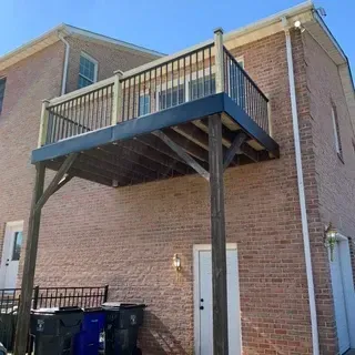 A wooden deck elevated by two support posts extends from the second story of a brick building above a back entrance.